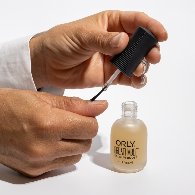 Person applying ORLY breathable calcium boost nail treatment with a brush on a white background